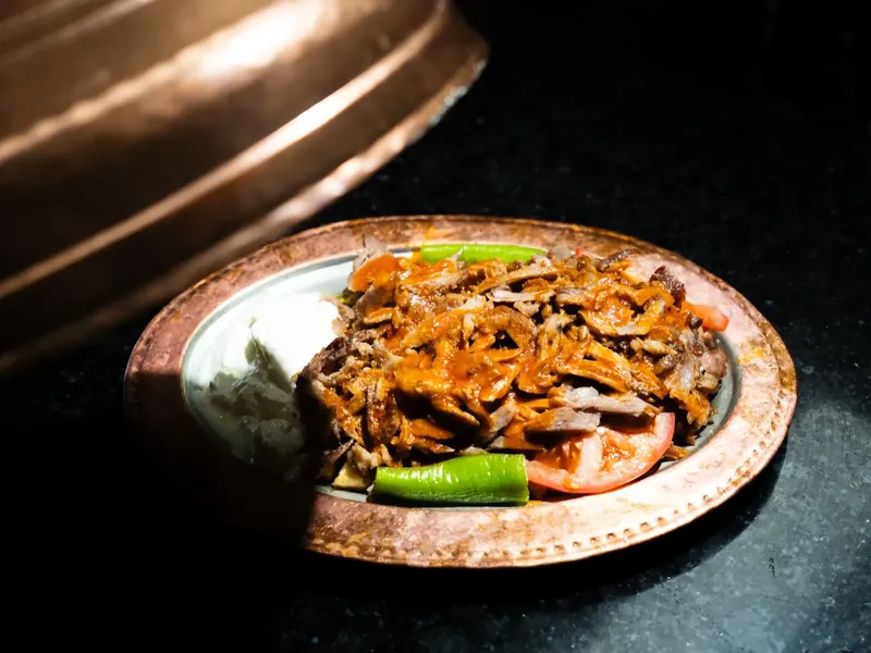 Après : une assiette d’iskender photographiée en lumière de studio, sur fond noir